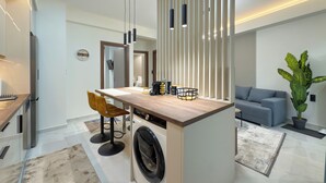A modern kitchen with a central island, a washing machine, and a dining area with two chairs. - Modern Muse Two-Bedroom Apartment (Thessaloniki)