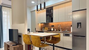 A modern kitchen with a built-in refrigerator, a dining area with a wooden table and yellow chairs, and a TV on a wooden cabinet. - Modern Muse Two-Bedroom Apartment (Thessaloniki)