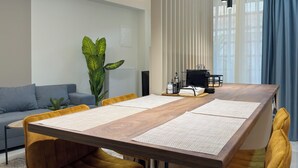 A modern meeting room with a long wooden table, yellow chairs, a potted plant, and a coffee machine. - Modern Muse Two-Bedroom Apartment (Thessaloniki)