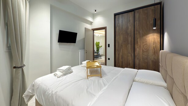 A modern bedroom with a bed, a ceiling fan, a TV, and a wooden wardrobe. - Modern Muse Two-Bedroom Apartment (Thessaloniki)