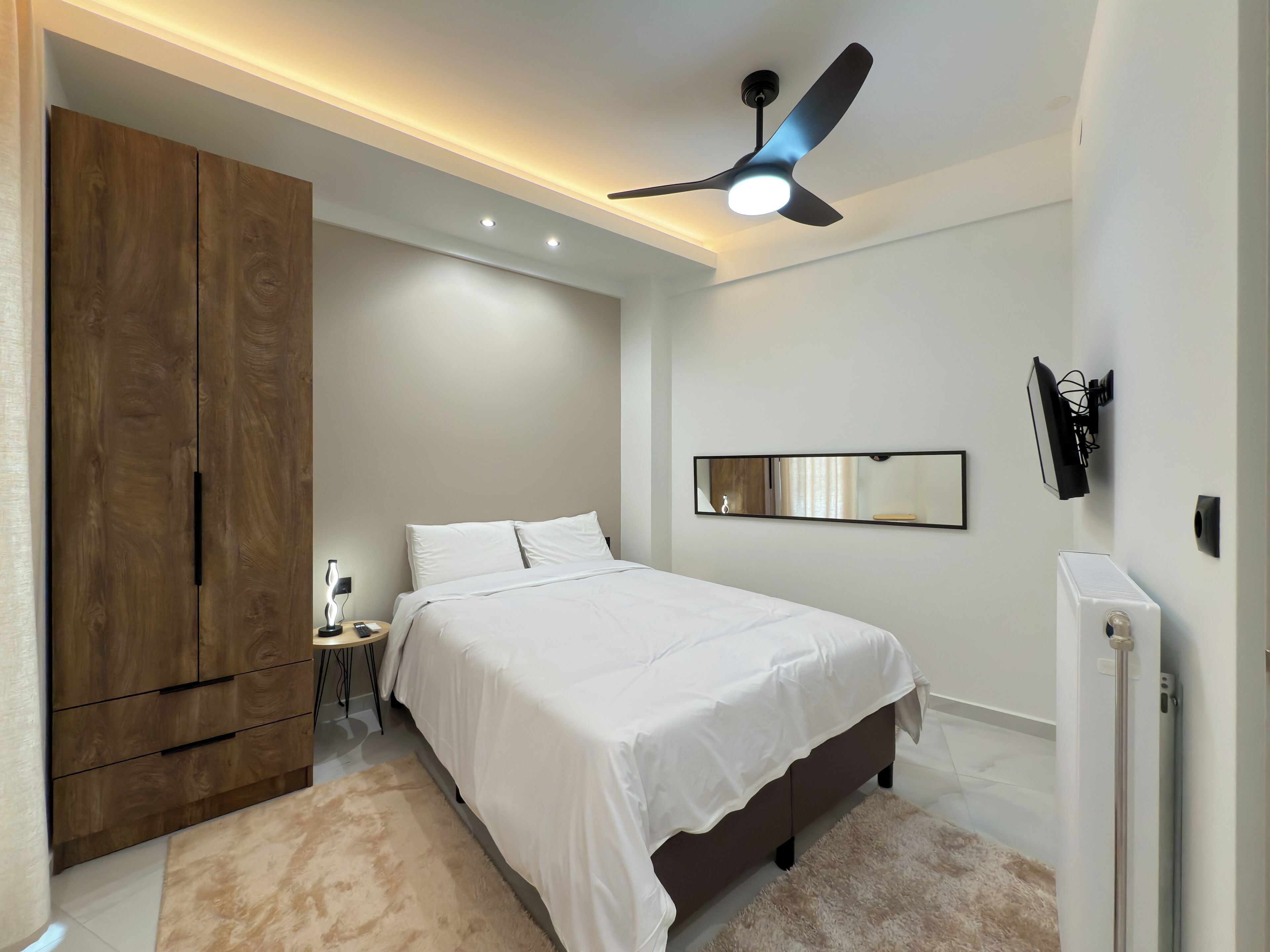 A bedroom with a bed, a wardrobe, a ceiling fan, a mirror, and a radiator.