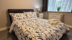 Une chambre à coucher avec un grand lit, une table de chevet, une commode, une fenêtre avec des rideaux et un tableau au mur.