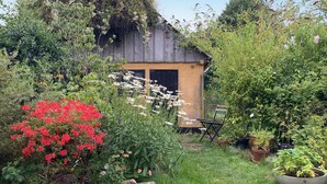Ein rustikaler Hollschuppen, umgeben von üppigem Grün und blühenden Pflanzen.