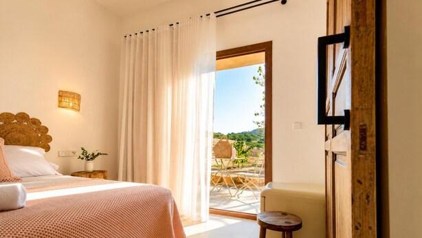 Quarto com cama, mesa de cabeceira, luminária, cadeira e vista para o exterior.