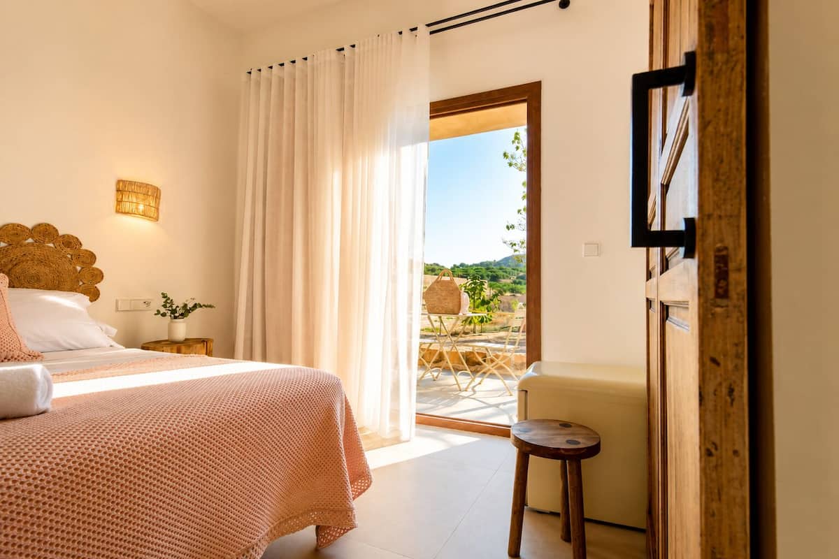 A bedroom with a bed, a nightstand, a lamp, a chair, and a view of the outdoors.