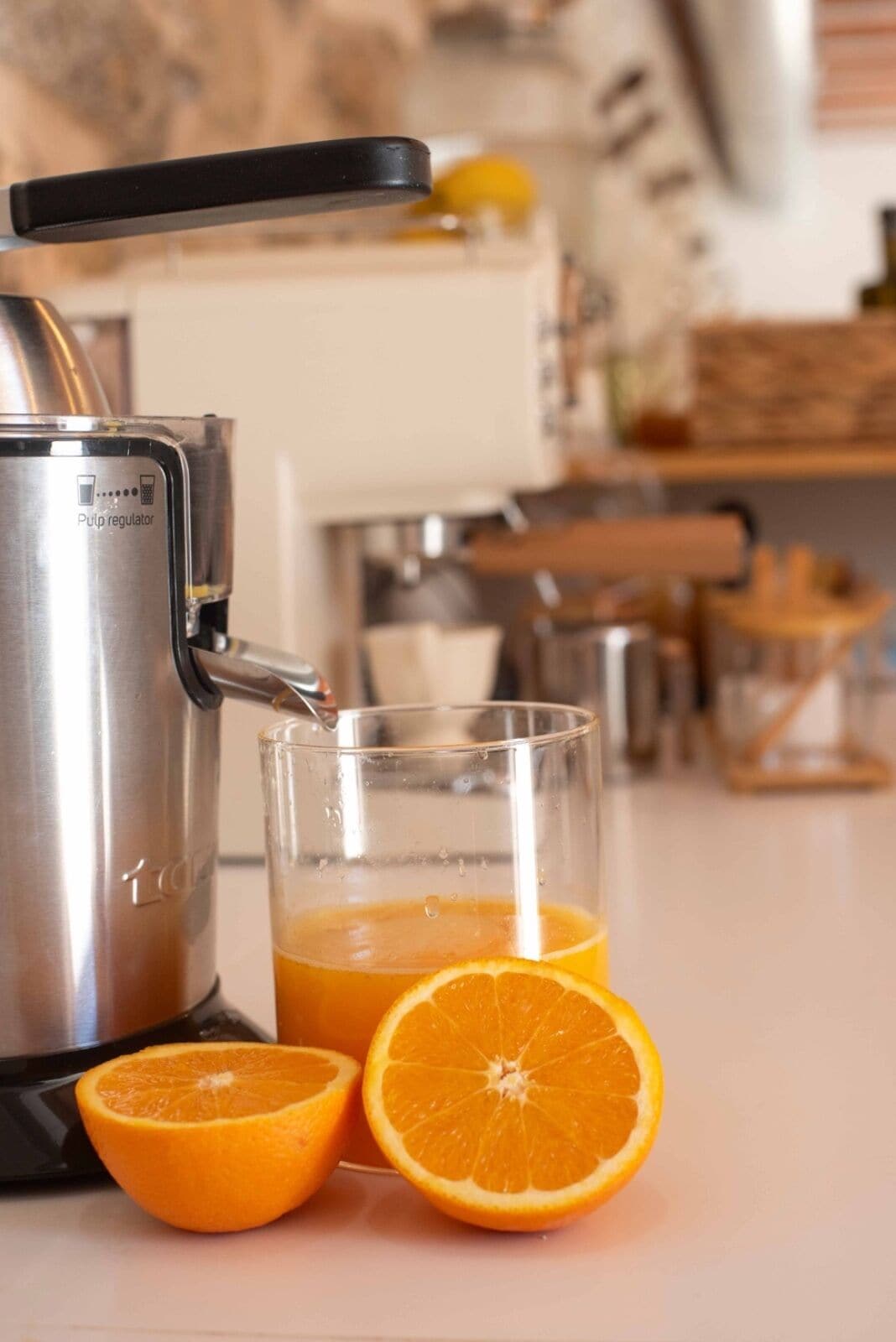 Una cocina con un exprimidor de jugos, un vaso de jugo y una naranja cortada por la mitad.