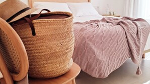 Quarto com cama, cadeira, cesta de vime e mesa de cabeceira com abajur.