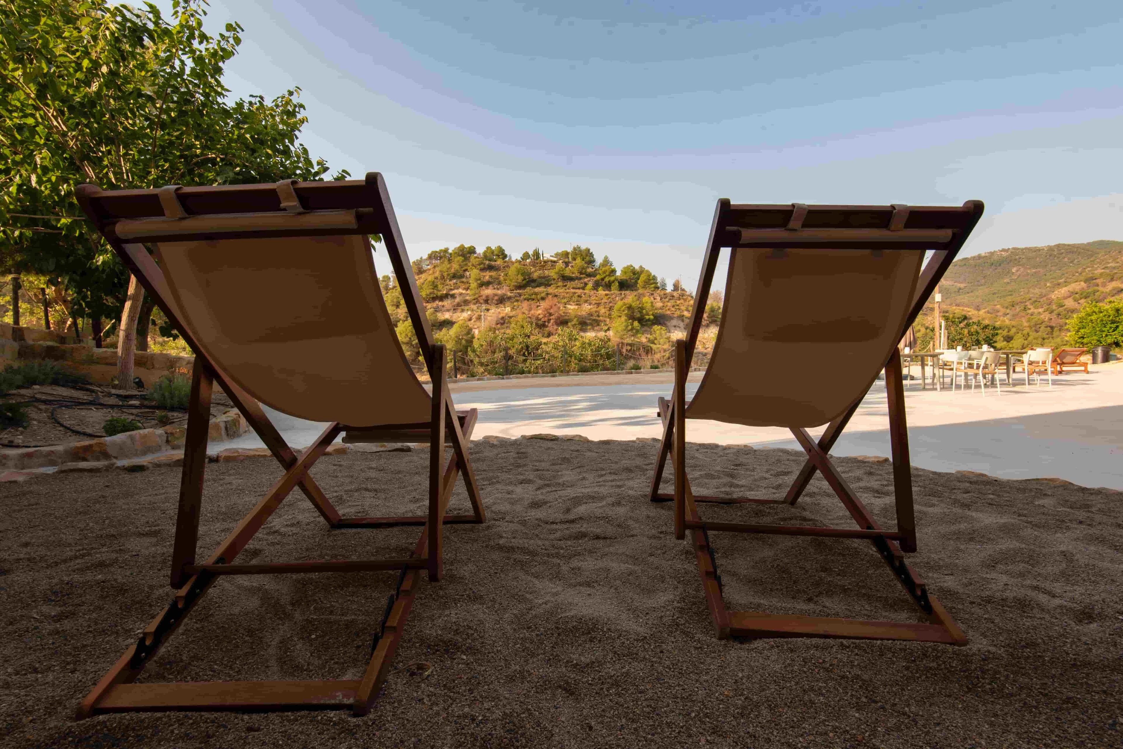 Two wooden beach chairs facing a beach with a view of a hilly landscape.