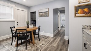 A dining area with a wooden table and chairs, a kitchen with grey cabinets, and a hallway leading to another room.