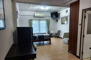 A room with a bed, a desk, a TV, and a window with curtains.