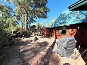 Eine rustikale Holzhütte mit einem Steinweg, der zu einer überdachten Grillstelle führt, umgeben von Bäumen und einem Holzzaun.