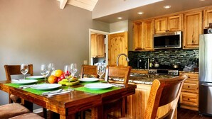 A modern kitchen with wooden cabinets, a stainless steel refrigerator, and a dining area with a wooden table set for four.