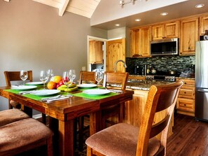 Una cocina moderna con armarios de madera, un refrigerador de acero inoxidable y una zona de comedor con una mesa de madera dispuesta para cuatro personas.