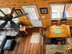 A cabin interior with a ceiling fan, a dining table, a sofa, and a kitchen area with a fruit bowl.