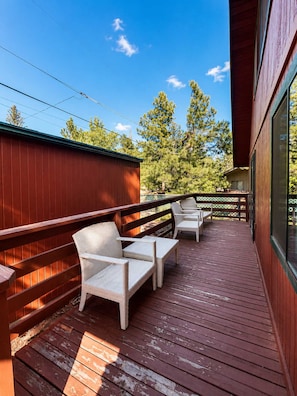A wooden deck with two wicker chairs and a table, overlooking a forested area.