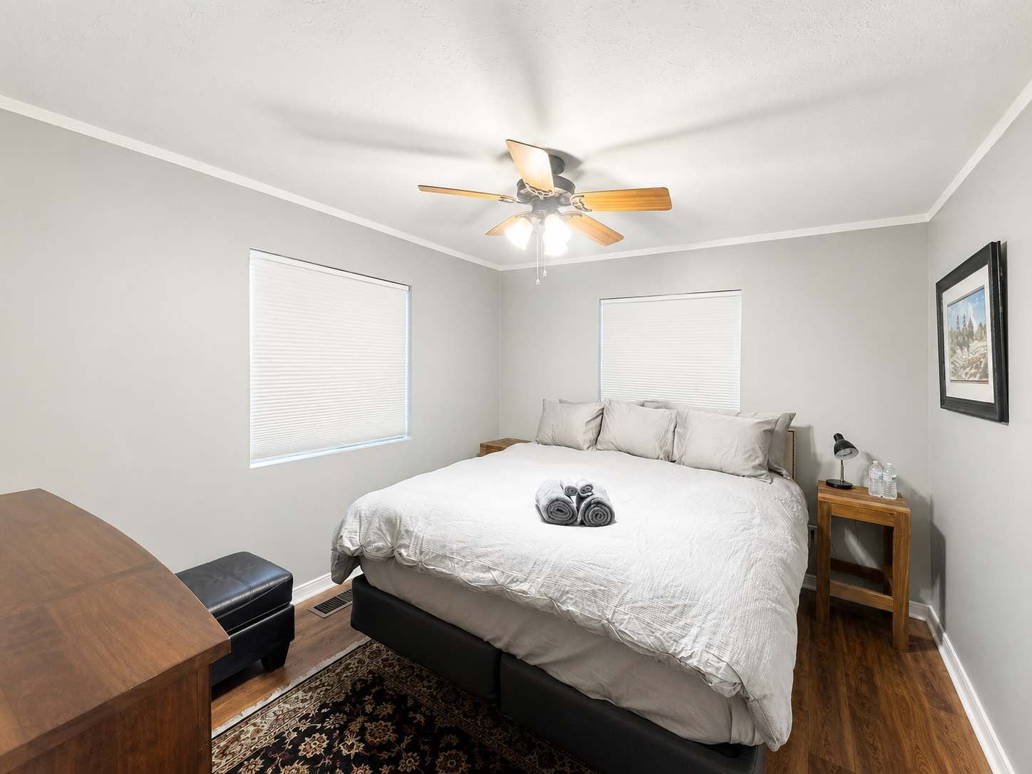 A bedroom with a bed, a ceiling fan, a nightstand with a lamp, and a framed picture on the wall.