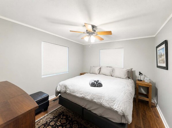 Une chambre à coucher avec un lit, un ventilateur de plafond, une table de chevet avec une lampe et un tableau encadré au mur.