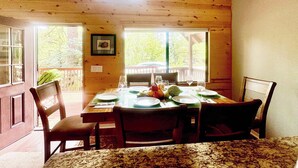 Comedor con mesa de madera dispuesta para cuatro personas, rodeada de sillas y vista a zonas verdes.
