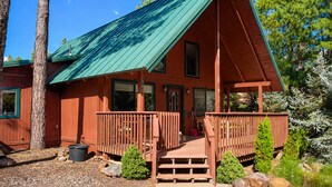 A cabin with a green roof, wooden deck, and a porch.