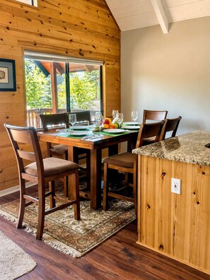 Un intérieur en bois avec une table à manger dressée pour quatre personnes, entourée de chaises, et un îlot de cuisine doté d’un plan de travail.