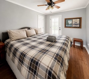 A bedroom with a large bed, a ceiling fan, a small table, and a framed picture on the wall.
