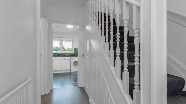 Un pasillo que da a una cocina con muebles blancos y una lavadora.