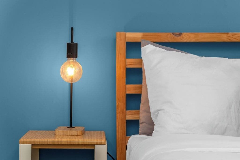 A bed with a wooden headboard, a bedside table with a lamp, and a blue wall.