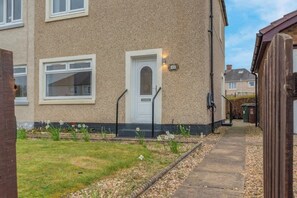 A residential building with a white door, windows, and a small garden with flowers and gravel. - Vacant Nests | The Grampian | Free Parking (North Lanarkshire)