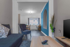 A modern living room with a sofa, a coffee table, a TV, and a dining area in the background.