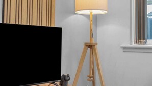 Una habitación con televisión, una lámpara de pie de madera y una ventana con persianas.