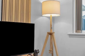 A room with a television, a wooden floor lamp, and a window with blinds.