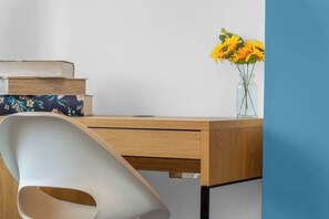 A desk with a vase of yellow flowers, a stack of books, and a modern chair. - Vacant Nests | The Grampian | Free Parking (North Lanarkshire)