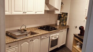 A compact kitchen with white cabinets, a granite countertop, a stainless steel sink, a gas stove, and a dishwasher.