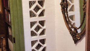 A hallway with a patterned floor, a decorative wall panel, a mirror with an ornate frame, and a small table with a basket and keys.