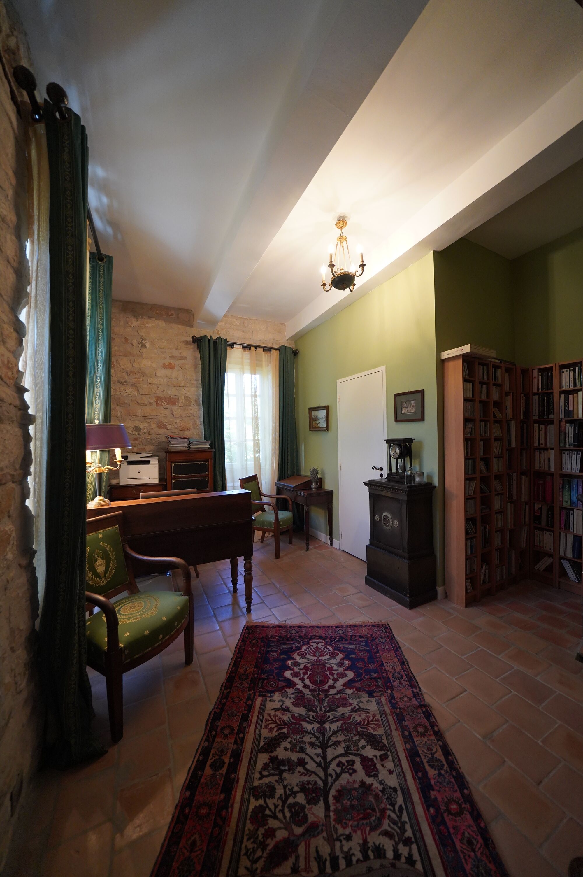 Une pièce comprenant un bureau en bois, une chaise, une bibliothèque, un tapis à motifs et un lustre.