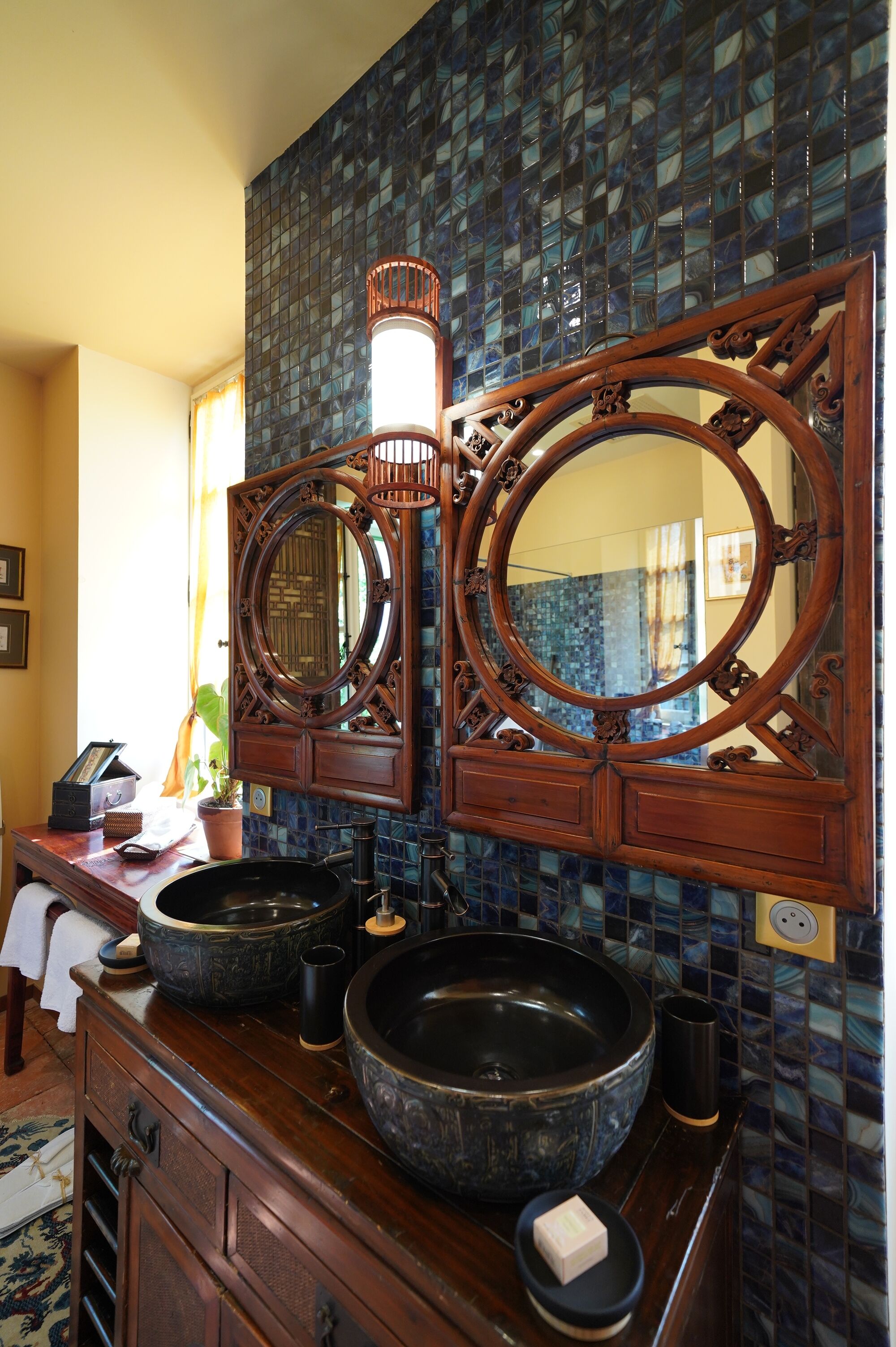 A bathroom with two large round mirrors, a wooden vanity, and a blue mosaic tile backsplash.