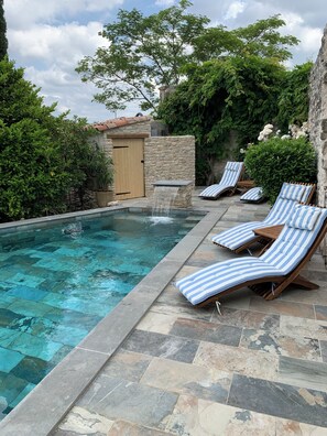 A swimming pool with a stone border and lounge chairs with striped cushions. - Chambres d'hôtes La Gourguille (Barjac)