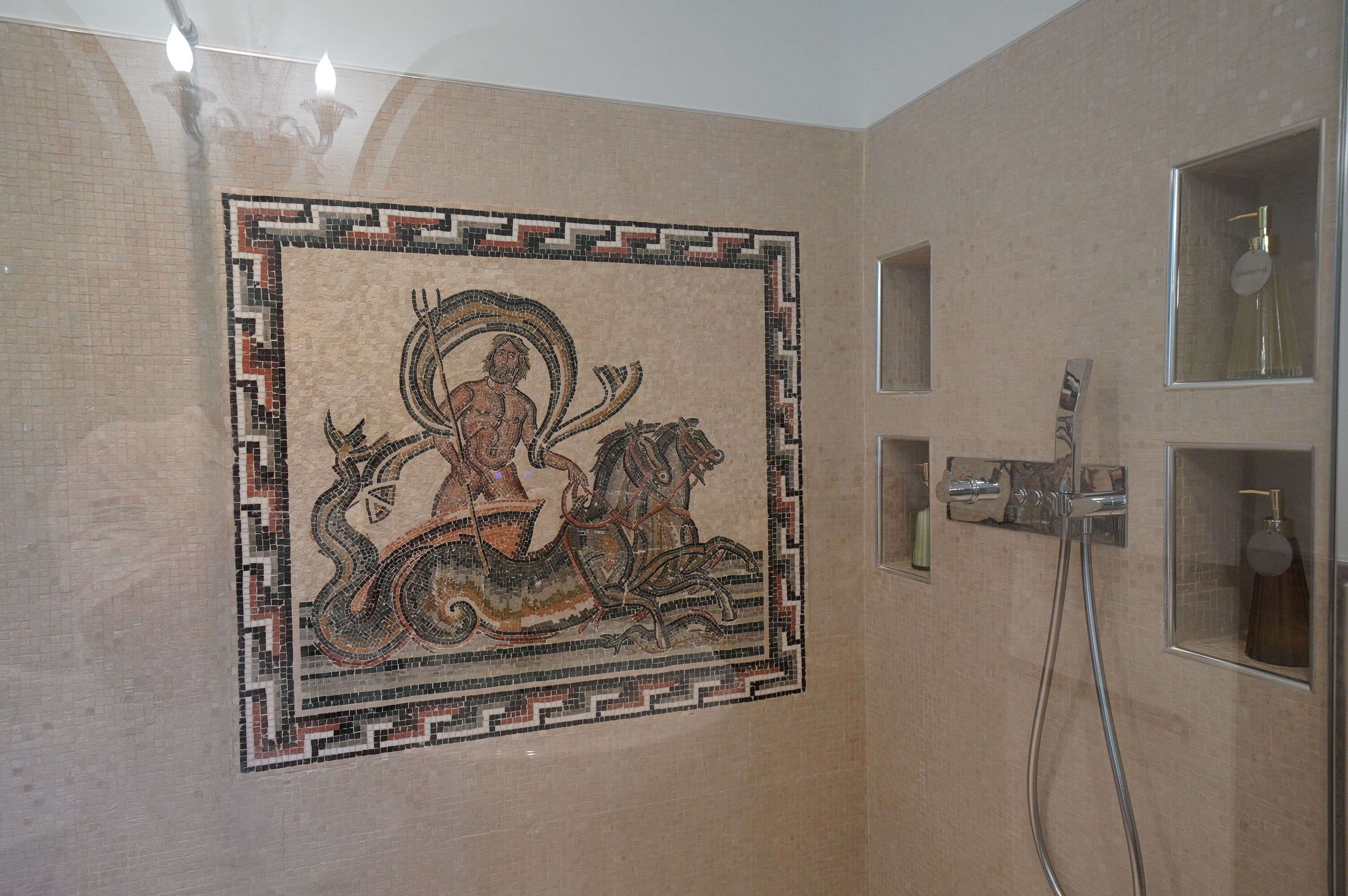 Una pared de mosaicos con una figura central a caballo, una zona de ducha con accesorios cromados y un estante pequeño con artículos de tocador.