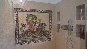 Una pared de mosaicos con una figura central a caballo, una zona de ducha con accesorios cromados y un estante pequeño con artículos de tocador.