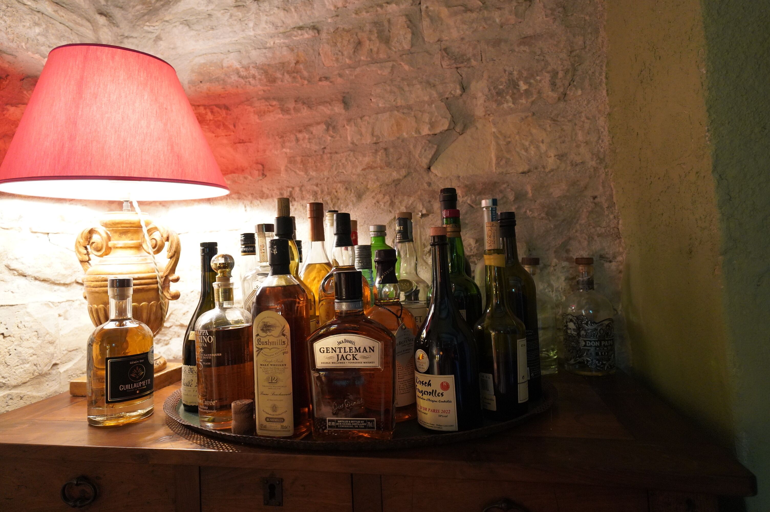Een verzameling drankflessen op een houten oppervlak, met een rode lamp op de achtergrond.