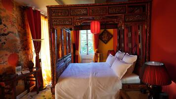 A traditional room with a large bed, ornate wooden headboard, and red curtains.