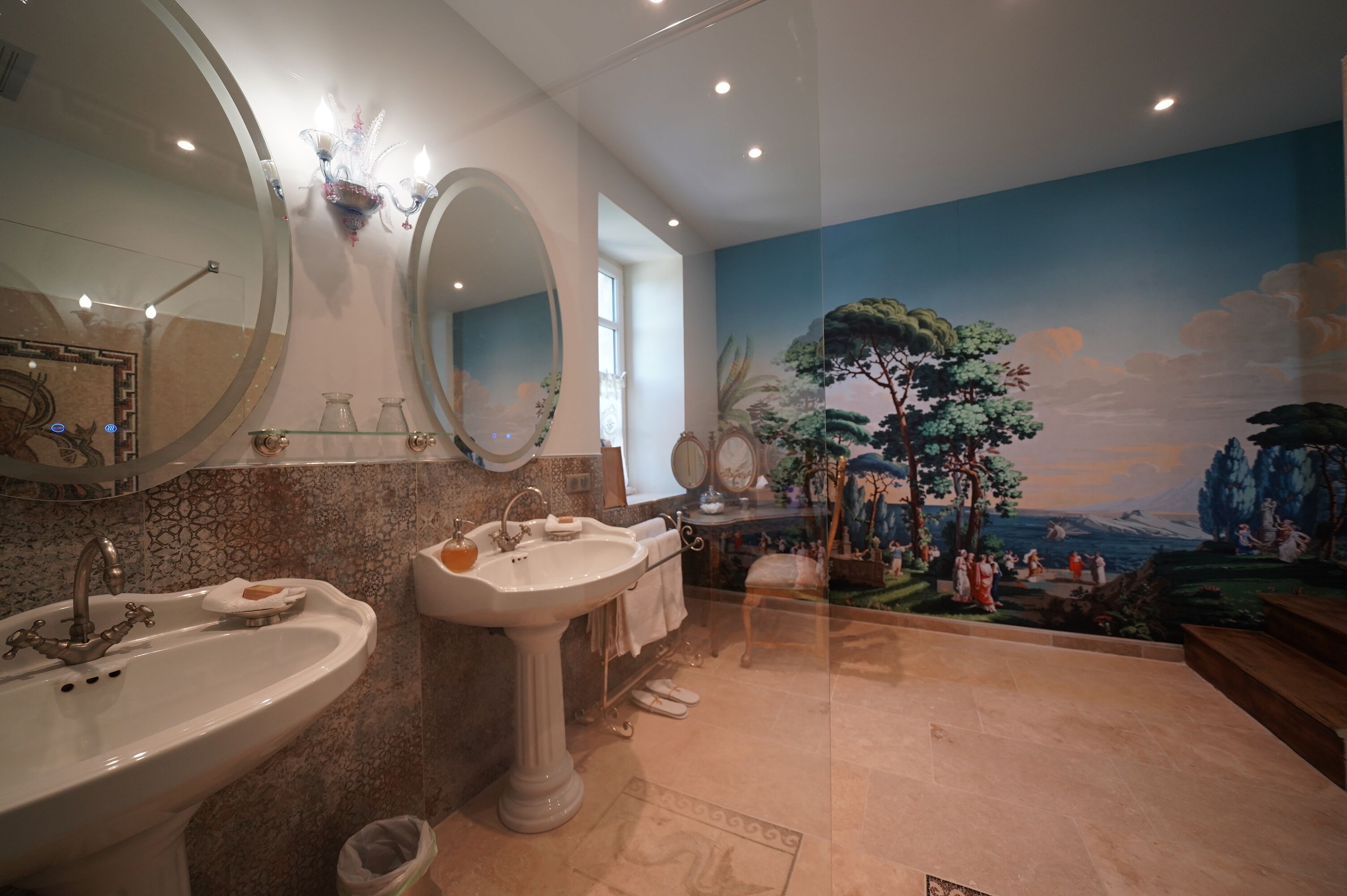Un baño con dos lavamanos, un espejo grande y un mural que representa un paisaje pintoresco.
