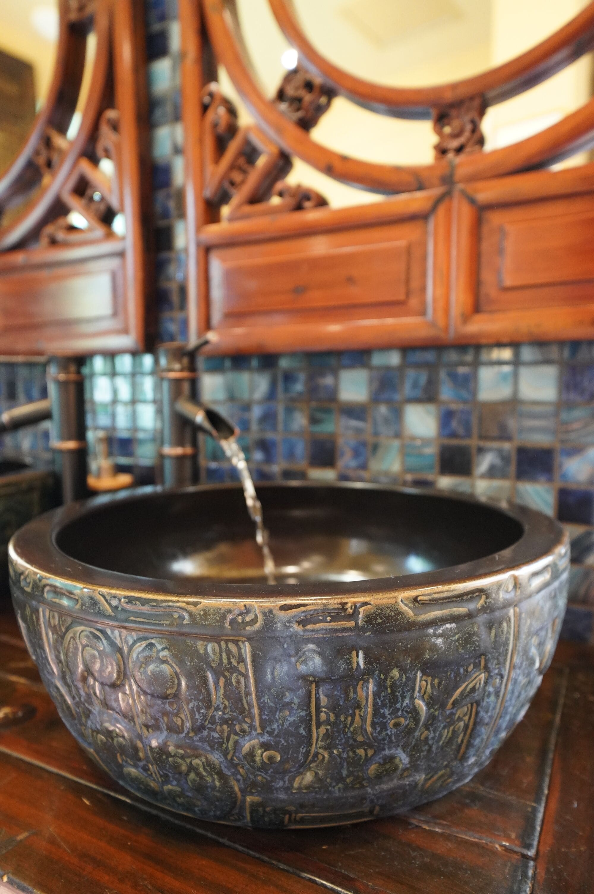 Una vasca metallica rotonda e decorata con acqua che vi scorre dentro, posata su un piano di legno.