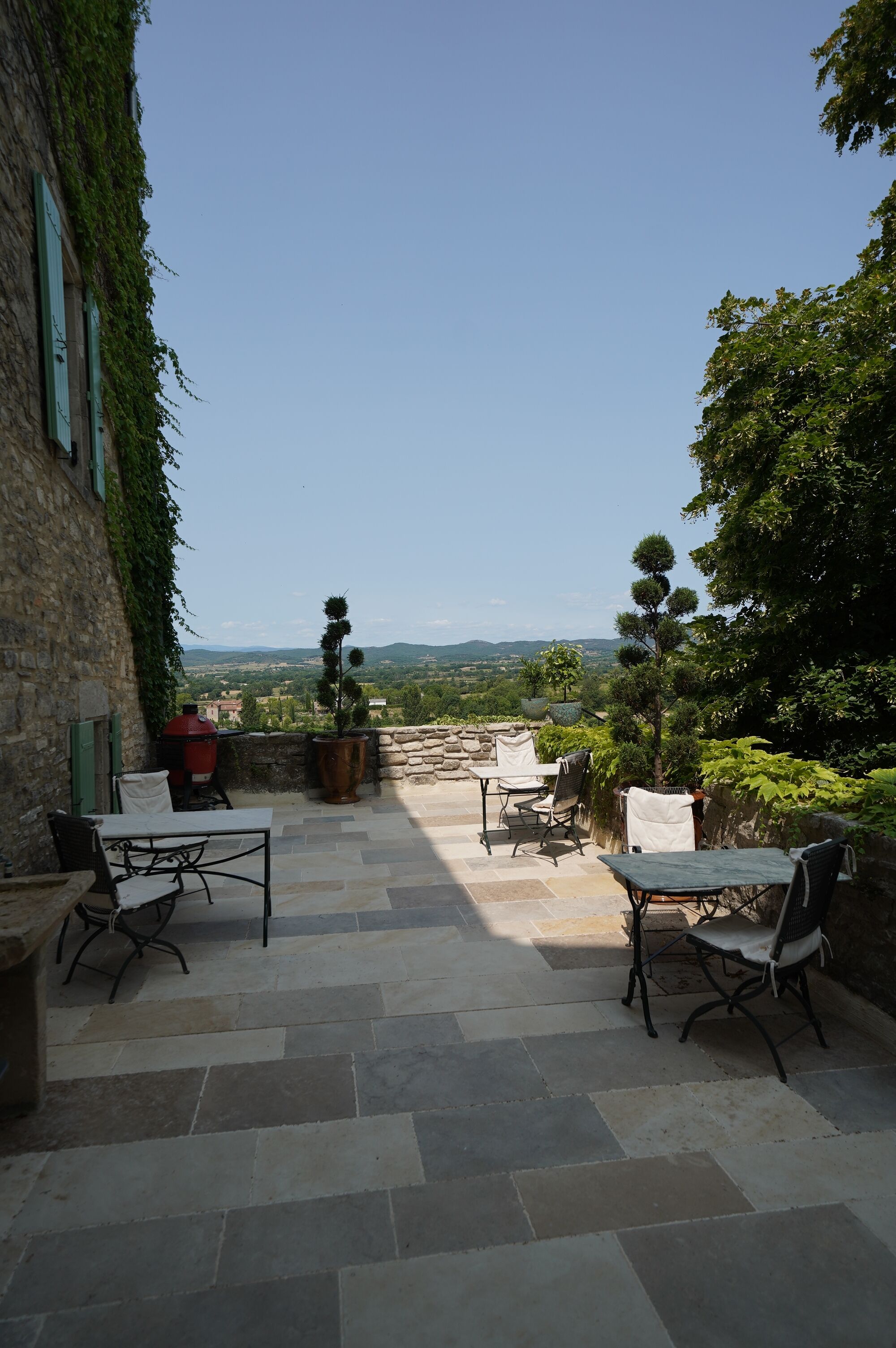 An outdoor patio with stone flooring, two tables, and four chairs.