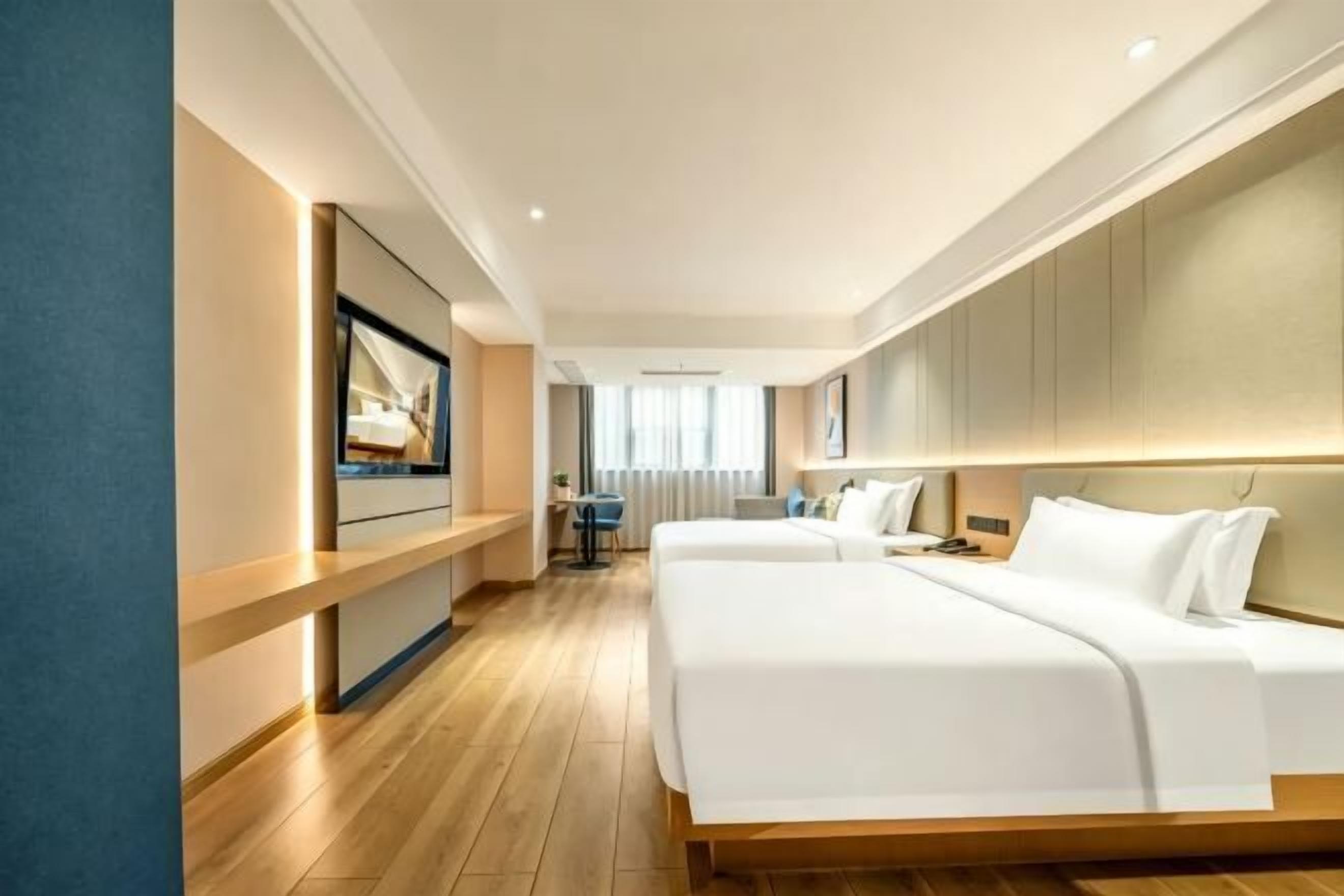 A hotel room with two beds, a TV, a desk, and a view of the city.