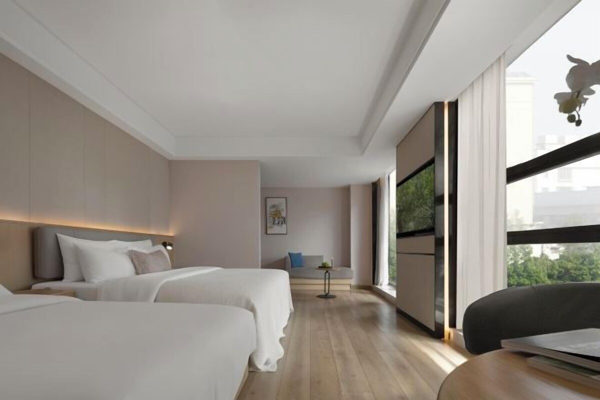 A hotel room with two beds, a desk, a chair, and a large window.