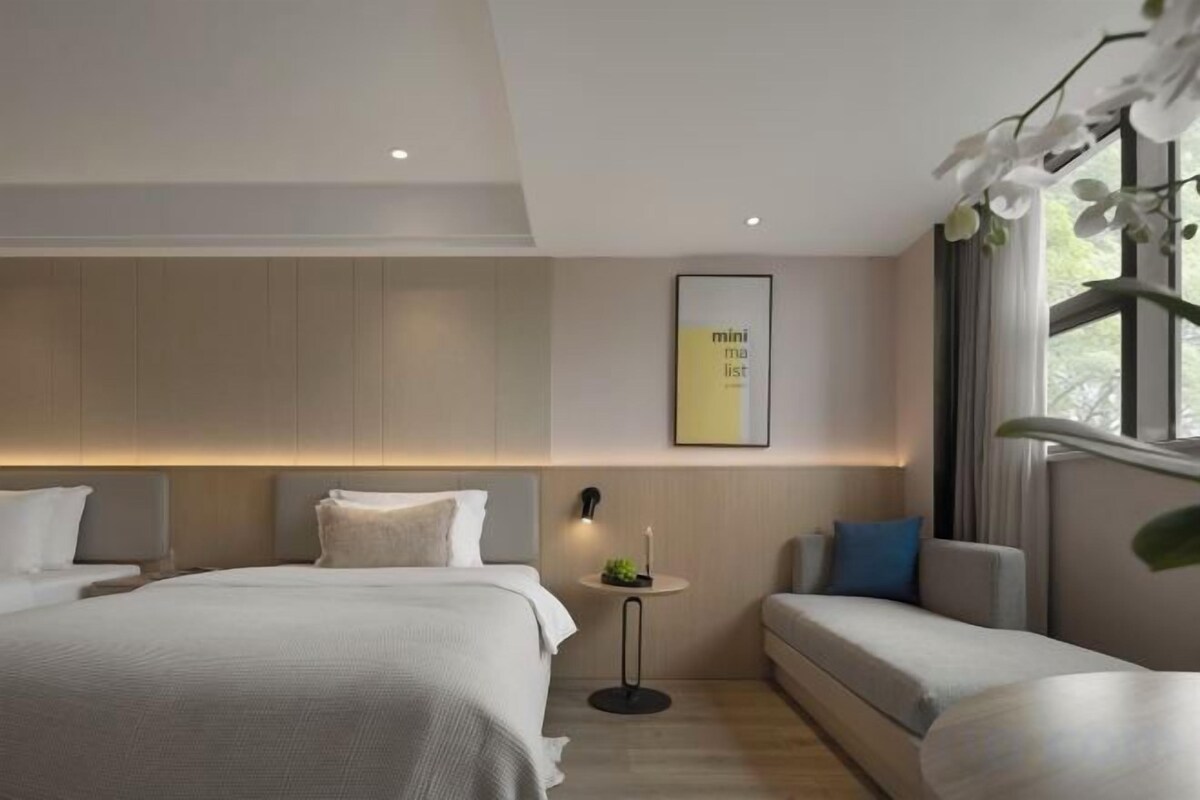 Una habitación de hotel moderna con una cama grande, un sofá, una mesita y un cuadro en la pared.