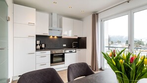 Una cocina moderna con armarios blancos, encimera oscura y una zona de comedor con dos sillas y una mesa.