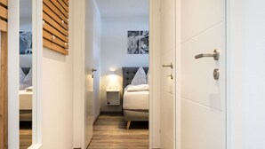 Un pasillo estrecho que conduce a un dormitorio con cama, mesita de noche y una obra de arte colgada en la pared.