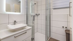Un baño moderno con cabina de ducha de vidrio, un lavabo blanco con lavamanos integrado y un espejo sobre el lavabo.